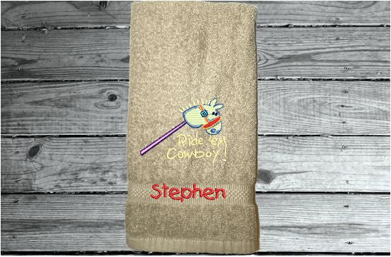 Beige hand towel 16" x 27" embroiderred stick horse with saying ride'em cowboy. You can personalize it with a name for a baby shower. Borgmanns Creations - 7