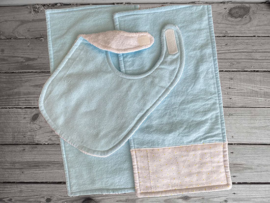 This bib and 2 burp cloths -baby blue color - one burp cloth has decorative strip of material across the end, blue and yellow dots on white background. Made of flannel top and terry cloth backing bib 9