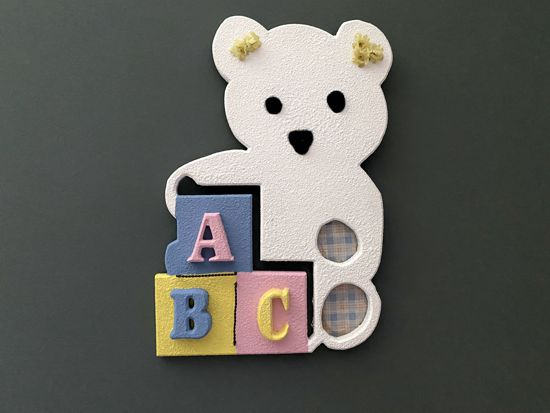 Wall hanging of a white teddy bear with color blocks cut from MDF board, panted with texture paint and top coat is white acrylic paint, eyes and nose are black pompoms, wire, flowers and material are added for finishing touches, hanger on back 12" x 15", makes a great design for you or a baby shower gift for a friend - Borgmanns Creations