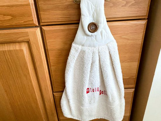 Beige kitchen hanging towel, embroidered words (Sleigh Bells) -  Christmas gift for mom for her kitchen decor -  can also be hooked over a bathroom cabinet handle - terry towel has a beige quilted top dark button 16" wide - 21" long - Borgmanns Creations - 1