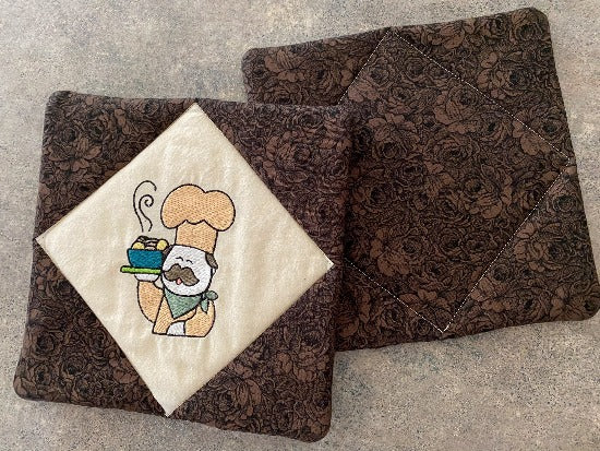 Pot holder set, 2 layers of Insul-Bright in the center, diamond shaped unbleached muslin with embroidered chef design,  brown floral pattern around design and on the back  7