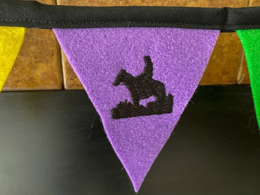 Trail rider banner, 11 flags each 3 1/2" x 4 1/2" of soft felt sewn to bias tape, Embroidered letters, Colors are yellow, purple and green with a trail rider on the center flag, The flag section is 42" and there is 2 ft of black bias tape on each side for tying. Great for the kids room. Photo prop  - Borgmanns Creations 