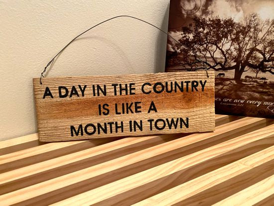 Wood sign wall hanging is cedar upcycled fence panel with the saying "A day in the country is like a month in town" ,hand painted, hung by wire, 11" x 4", would be a unique one of a kind house warming gift, birthday, wedding shower, wedding gift etc. The natural wood color will go with any room -Borgmanns Creations 