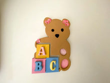 Load image into Gallery viewer, Baby shower gift - wood wall art teddy bear - wall hanging boy/ girl nursery decor - Shelf sitter or leaning against a wall at floor level. - this woodland nursery theme teddy bear is textured painted -  pink flowers ion the ears and pink feet bottoms - pompom eyes and nose, - colorful ABC blocks - hanging hook on back - Borgmanns Creations
