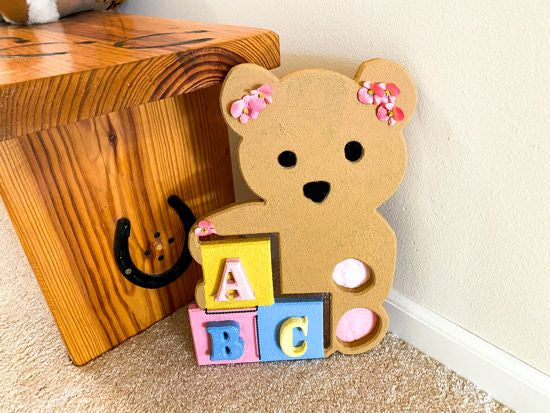 Baby shower gift - wood wall art teddy bear - wall hanging boy/ girl nursery decor - Shelf sitter or leaning against a wall at floor level. - this woodland nursery theme teddy bear is textured painted - pink flowers ion the ears and pink feet bottoms - pompom eyes and nose, - colorful ABC blocks - hanging hook on back - Borgmanns Creations