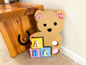 Baby shower gift - wood wall art teddy bear - wall hanging boy/ girl nursery decor - Shelf sitter or leaning against a wall at floor level. - this woodland nursery theme teddy bear is textured painted - pink flowers ion the ears and pink feet bottoms - pompom eyes and nose, - colorful ABC blocks - hanging hook on back - Borgmanns Creations