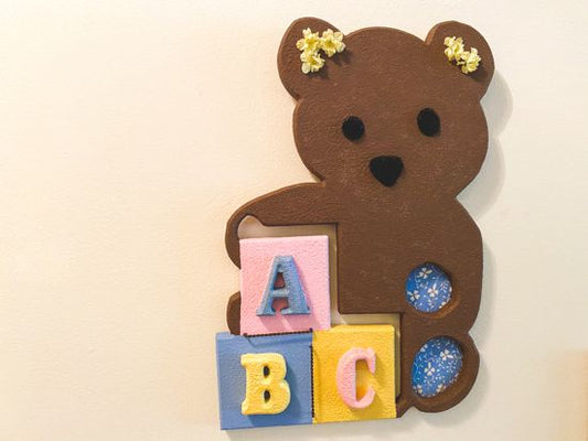 Wood wall art wall hanging, 1/2" MDF board, layered wood, hand painted brown, with wire, pompom balls, flowers and hanging hook on the back, 14" H x 10" W x 1/2" D, this wood sculpture of a brown teddy bear would be a great baby shower gift for the farmhouse decor or even leaning against a wall at floor level - Borgmanns Creations 