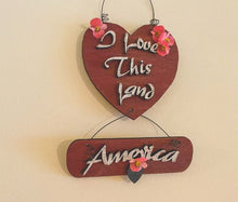 Load image into Gallery viewer, Wood wall hanging &quot; I love this Land America&quot;, laser cut Luan wood, wire attaches top heart to second piece, letters cut from luan wood, acrylic paint, glued together, flowers to complete the wall art, .12&quot; x 7&quot; including wire hanger, a great home decor gift for a veteran for his den or study - Borgmann Creations 

